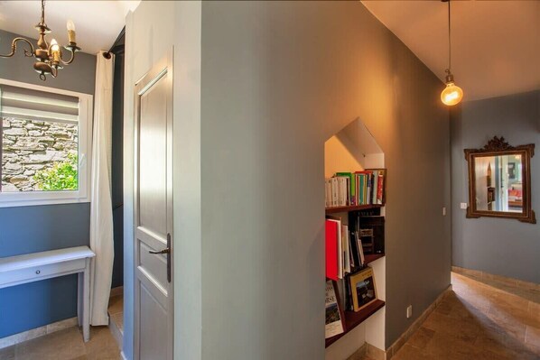 A hallway with a bookshelf, a bench, and a stone wall. - Villa Merusellu (Sisco)