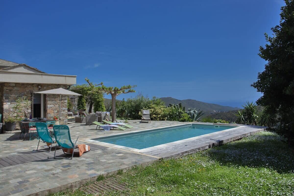 Zona de piscina con patio de piedra, sillas de descanso y vistas a las montañas.