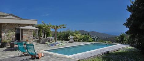 Zona de piscina con patio de piedra, sillas de descanso y vistas a las montañas.