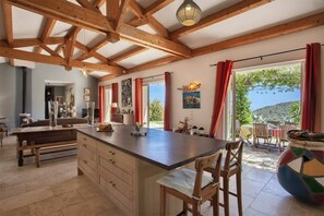 A spacious kitchen with wooden beams, a large island, and a view of the outdoors. - Villa Merusellu (Sisco)