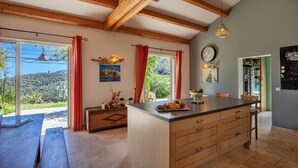 A spacious kitchen with wooden beams, a large island, and a view of the outdoors. - Villa Merusellu (Sisco)