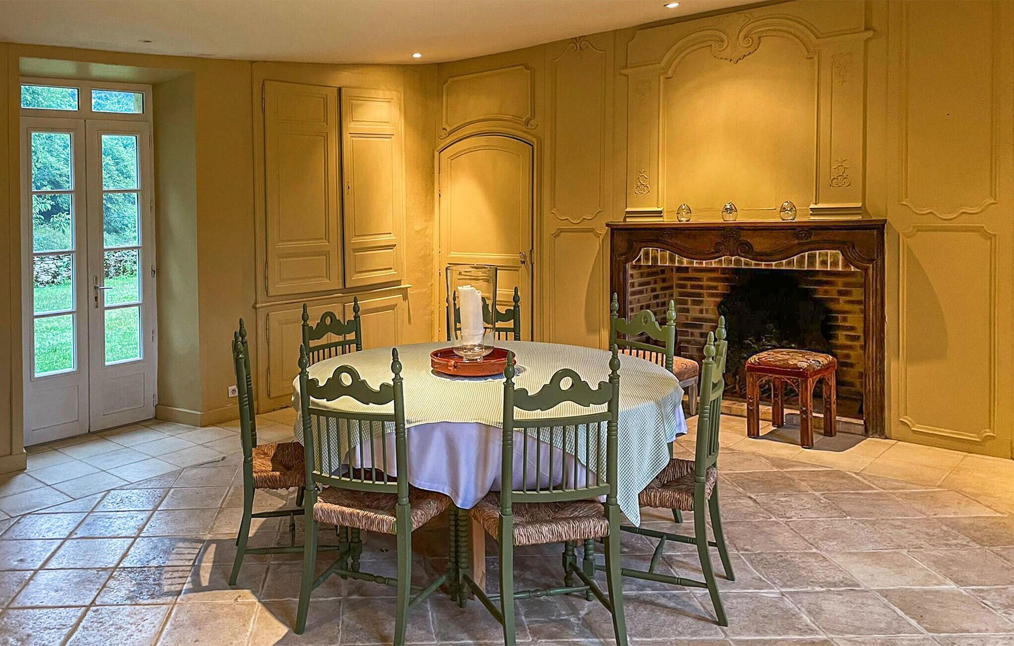 A dining room with a round table, green chairs, and a fireplace.