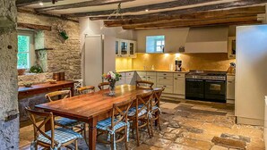 A rustic kitchen with stone walls, wooden beams, a dining table with chairs, and a stove. - Gorgeous home in Sarrazac (Sarrazac)