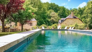 A rectangular swimming pool with a stone edge, surrounded by lush greenery and two stone buildings with pitched roofs. - Gorgeous home in Sarrazac (Sarrazac)