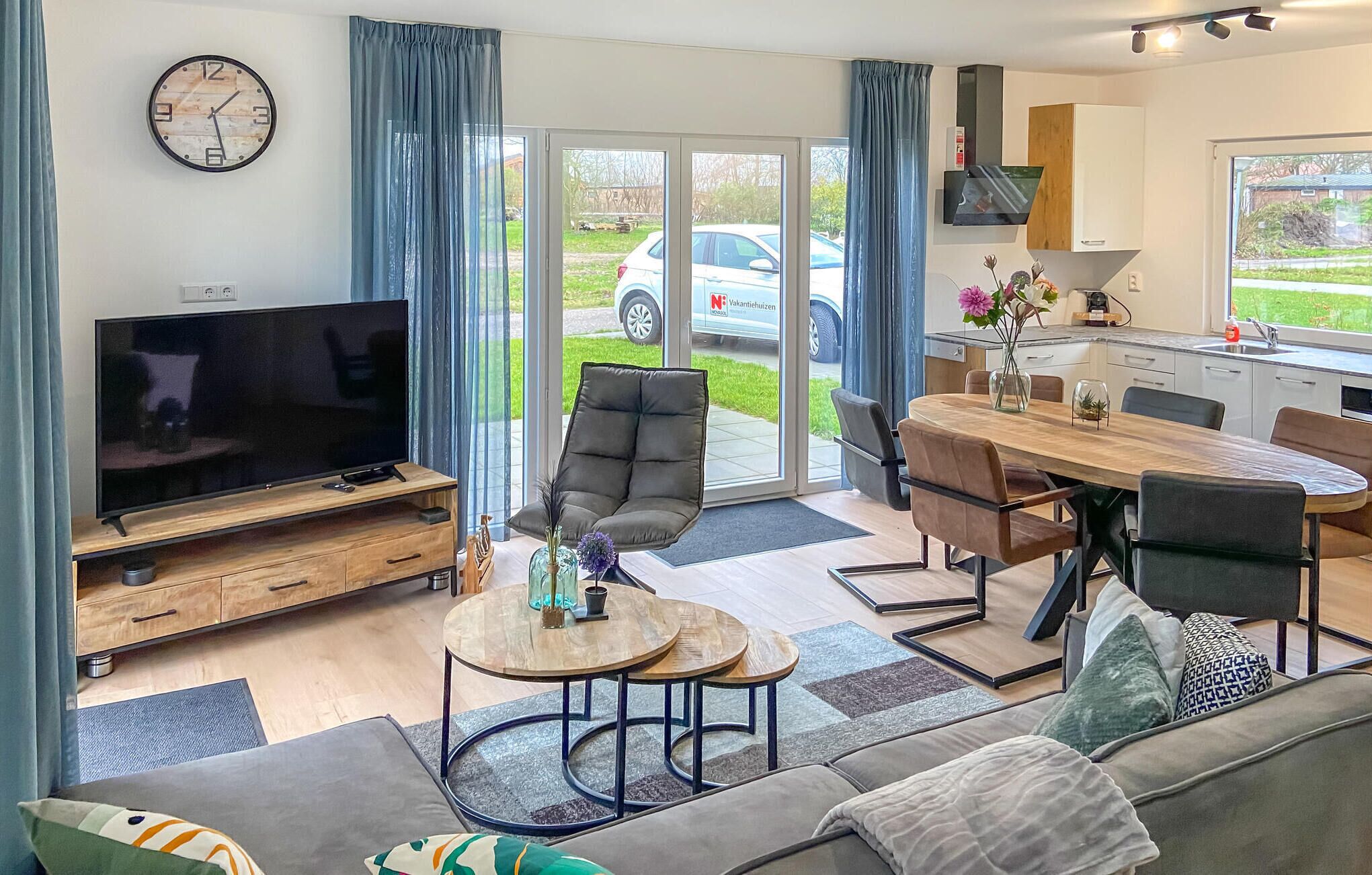 A modern living room with a flat-screen TV, a sofa, a dining table with chairs, and a kitchen area with a sink and cabinets.