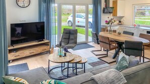 Una sala de estar moderna con un televisor de pantalla plana, un sofá, una mesa de comedor con sillas y una cocina con fregadero y armarios.