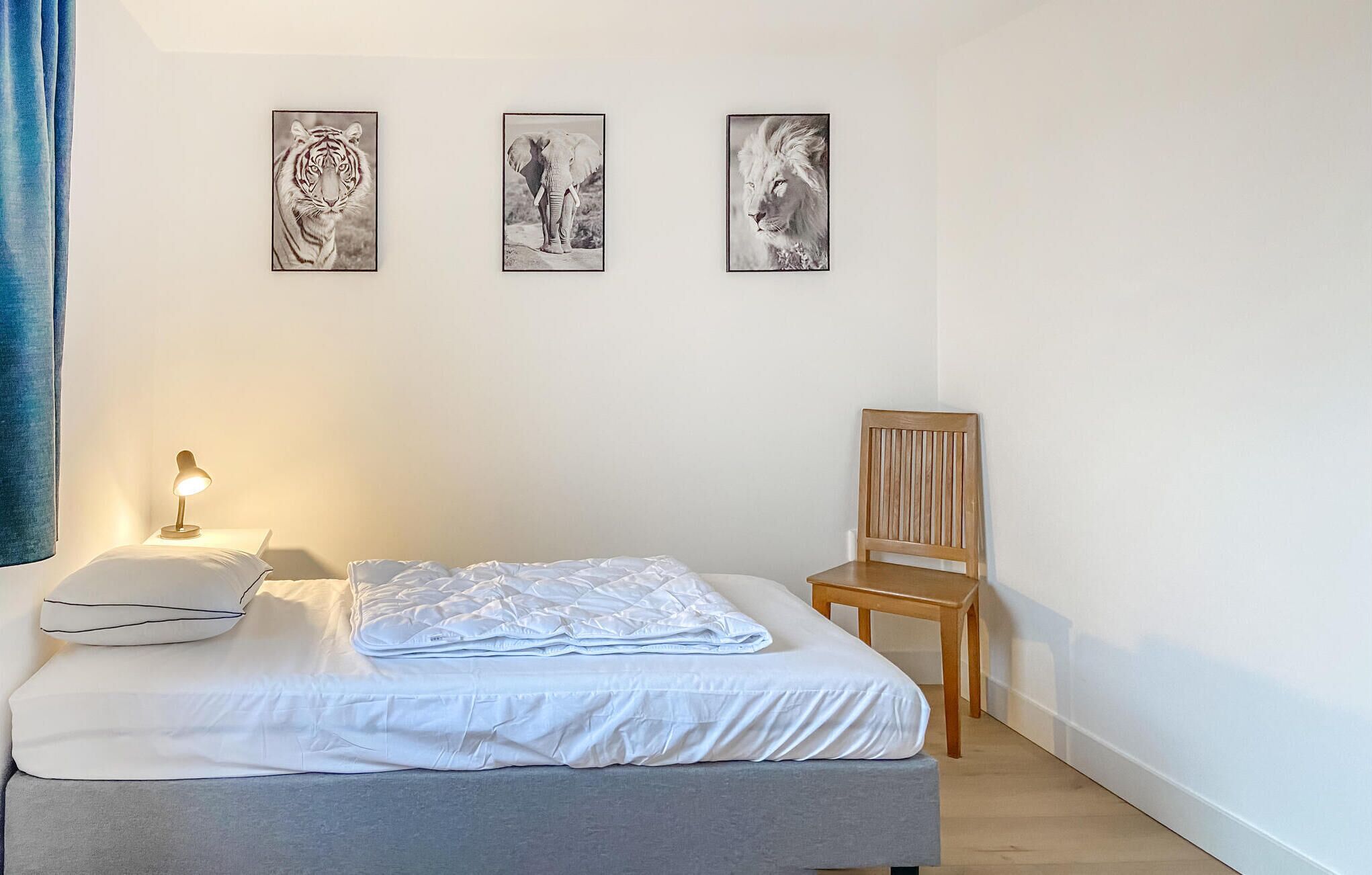 A bedroom with a bed, a bedside lamp, a chair, and three framed animal pictures on the wall.