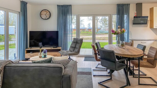 Una sala de estar moderna con televisor de pantalla plana, asientos cómodos, comedor y ventanas amplias con vistas al exterior.