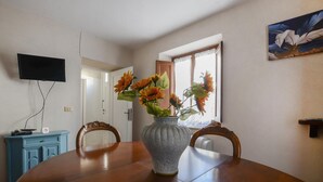 A dining area with a round table, two chairs, a vase with flowers, a television mounted on the wall, and a window with curtains. - 2 bedroom lovely home in Valpromaro (Valpromaro)