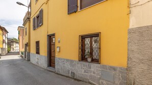 A narrow street with a yellow building featuring a stone base, a wooden door, and a window with a metal grille. - 2 bedroom lovely home in Valpromaro (Valpromaro)