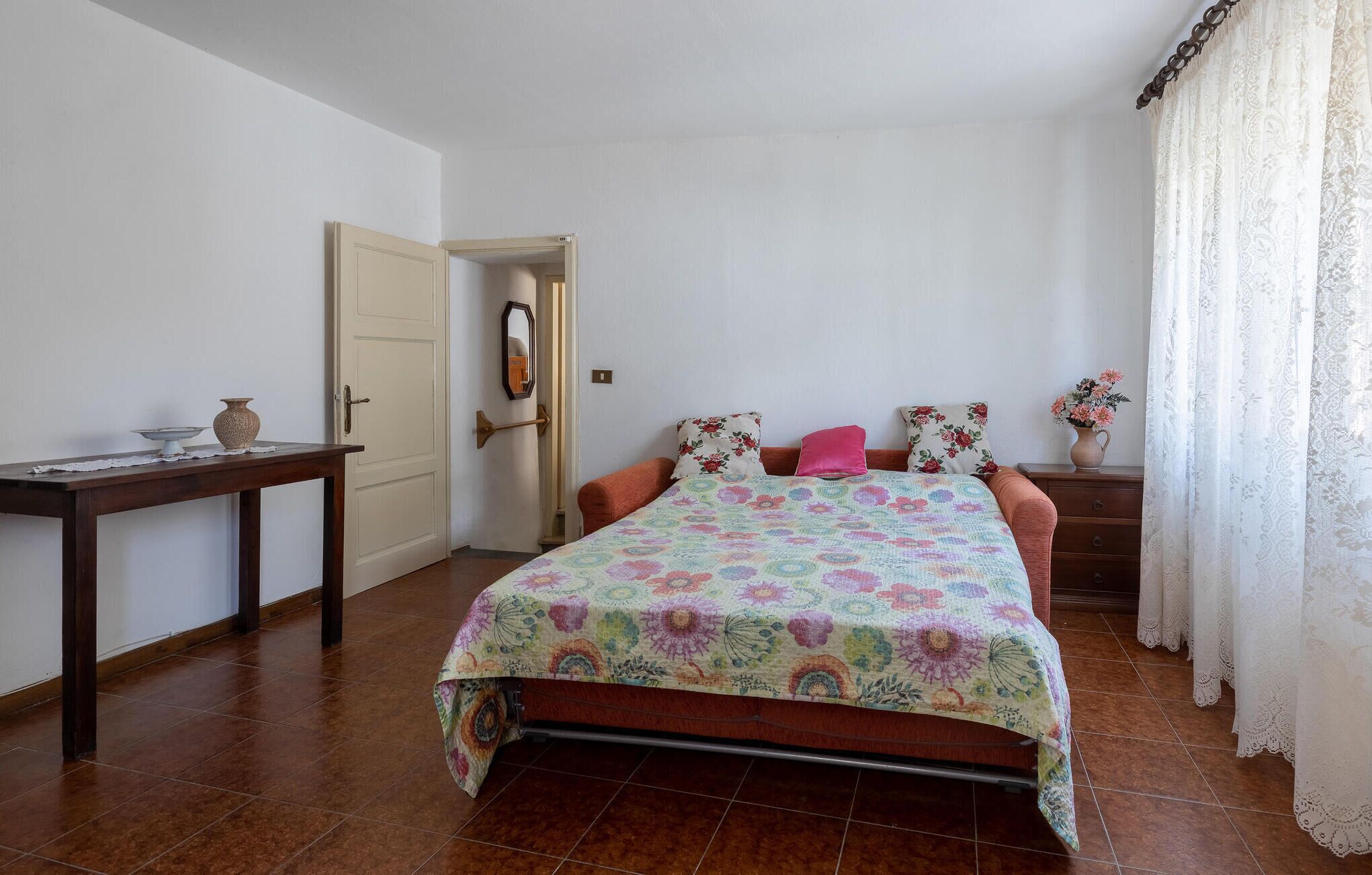 A bedroom with a bed, a nightstand, a dresser, a door, and a mirror.