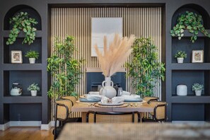 A dining area with a table set for four, surrounded by wicker chairs, with potted plants on shelves and a large vase of pampas grass in the center. - LUX 8BR/4BA Villa w/Heated Pool+Spa, 5min to Strip (Las Vegas)