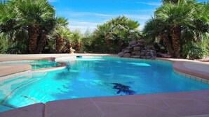 Ein Swimmingpool mit klarem, blauem Wasser, umgeben von Palmen und einem Steinbau.