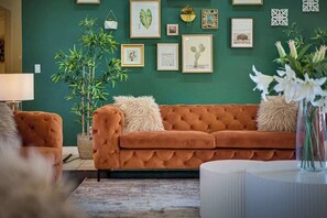 A living room with a tufted sofa, a potted plant, and framed artwork on the wall. - LUX 8BR/4BA Villa w/Heated Pool+Spa, 5min to Strip (Las Vegas)