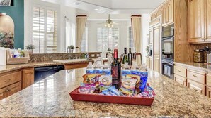 Eine Küche mit Granit-Arbeitsplatten, Holzschränken, einer zentralen Kochinsel mit Snacks und Getränken sowie einem Blick auf die Stadt durch große Fenster.