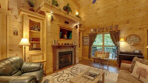 A cozy cabin interior with a fireplace, leather sofa, wooden coffee table, and a bookshelf.