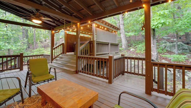 A wooden deck with a table and chairs, a staircase, and a view of the forest.