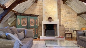 A cozy loft-style living room with a stone wall, a fireplace, a green cabinet, and a sofa with patterned cushions. - Nice home in Sarrazac (Sarrazac)