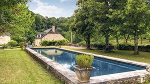 A swimming pool with a stone border, surrounded by a well-maintained lawn and trees. - Nice home in Sarrazac (Sarrazac)