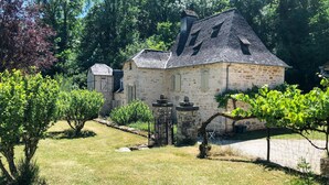 A stone house with a sloped roof, surrounded by a well-maintained garden with various shrubs and a vine-covered trellis. - Nice home in Sarrazac (Sarrazac)