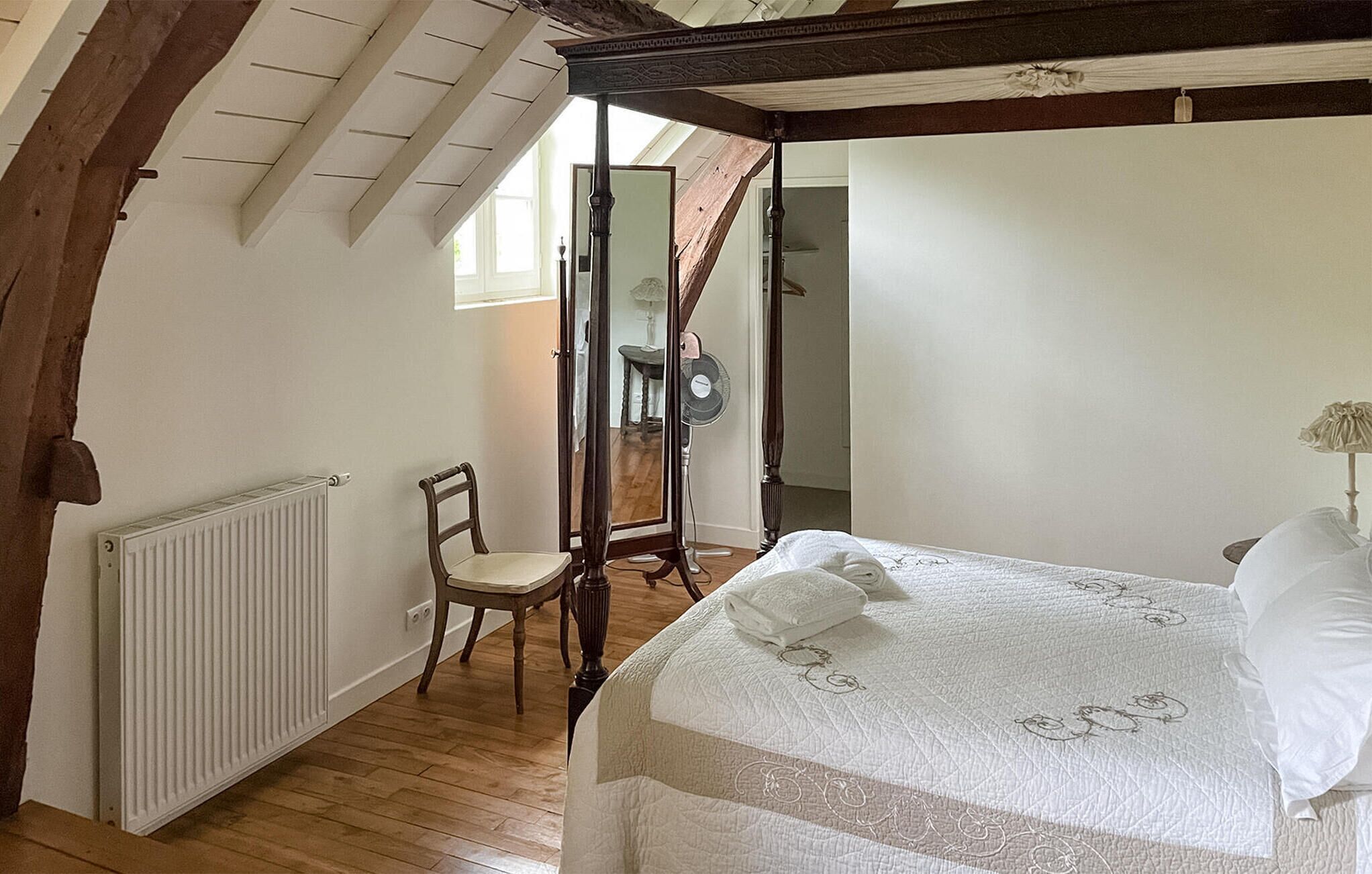A bedroom with a bed, a chair, a radiator, and a mirror.