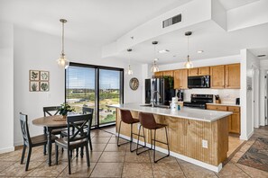 A modern kitchen with a central island, wooden cabinets, and stainless steel appliances. - Origin 803: Gulf-View 1BR w/ Sunset Corner Balcony! (Panama City Beach)