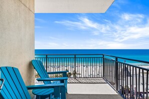 Un balcon avec deux chaises, une vue sur la plage et un ciel dégagé.