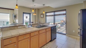 A modern kitchen with a large island, built-in dishwasher, and a view of the ocean through large windows. - Origin 803: Gulf-View 1BR w/ Sunset Corner Balcony! (Panama City Beach)