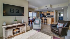 A spacious living room with a flat-screen TV, a wooden entertainment unit, and a comfortable seating area with a brown leather sofa and armchairs. - Origin 803: Gulf-View 1BR w/ Sunset Corner Balcony! (Panama City Beach)