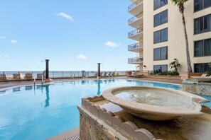 Une piscine dotée de chaises longues et d’une fontaine, entourée d’un immeuble de grande hauteur avec des balcons.