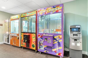 Eine Reihe von bunten Spielautomaten, darunter 'Toy Chest' und 'Prize Door', neben einem Geldautomaten.