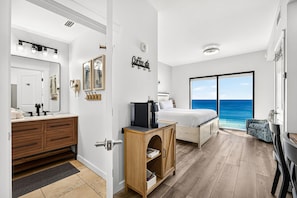 A hotel room with a large bed, a bathroom with a vanity, and a view of the ocean.