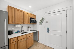 A kitchen with wooden cabinets, a microwave, a sink, and a door with a handle.