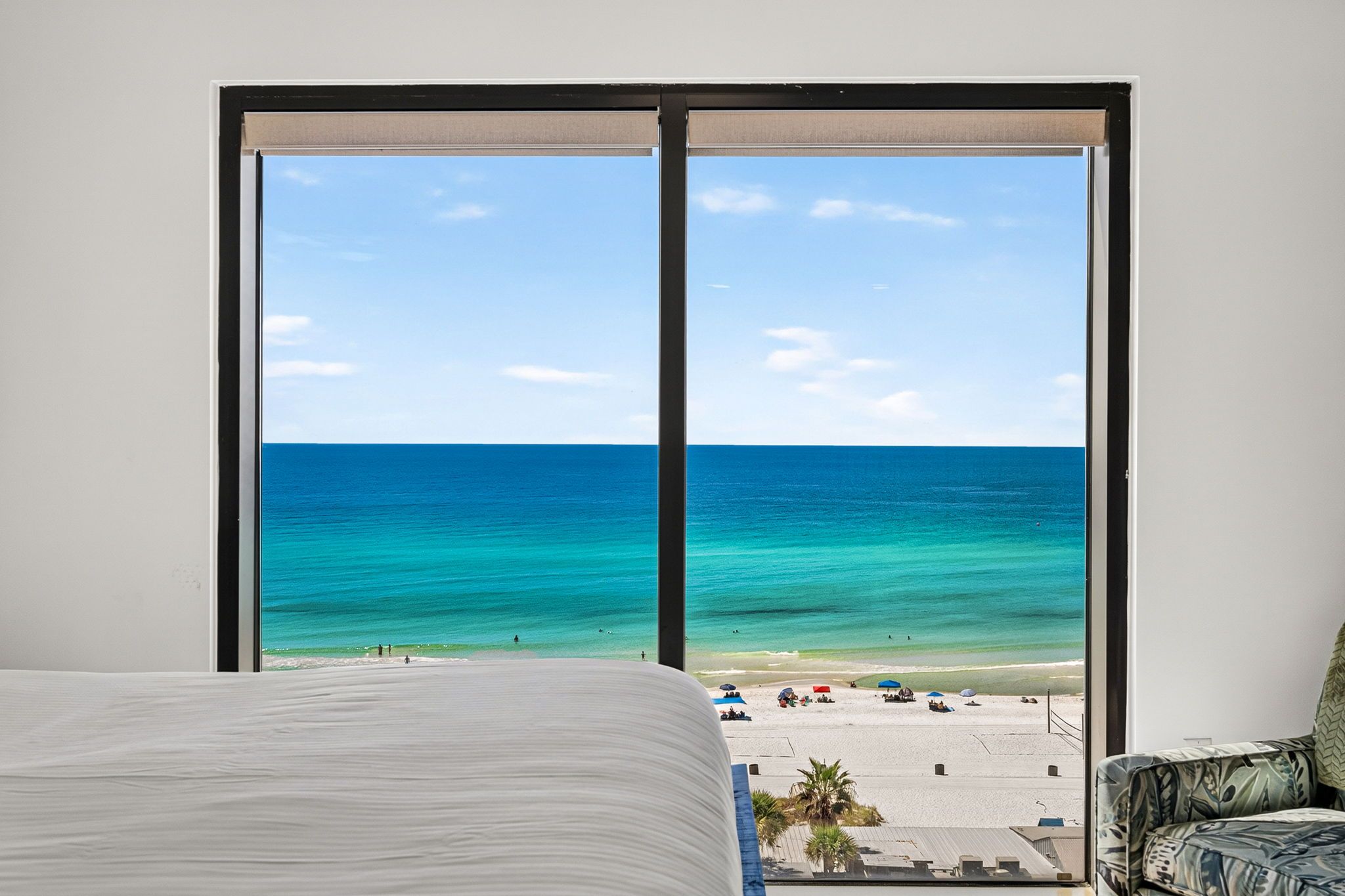 Ein Zimmer mit großem Fenster und Blick auf einen Strand mit klarem, blauem Wasser und Sand.