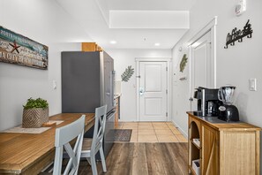 A compact kitchen with a dining area, a refrigerator, a coffee machine, and a decorative sign on the wall.