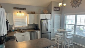 A kitchen with white cabinets, a stainless steel refrigerator, a sink, and a dining area with a table and chairs. - ~Tipsy Turtle~ Beautiful house in Ocean Lakes Campground with golf cart!  (Myrtle Beach)