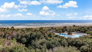 A beachfront property with a swimming pool, lush greenery, and a view of the ocean.