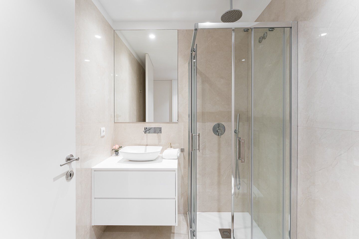 Une salle de bain moderne avec une douche à parois de verre, un lavabo blanc et un miroir au-dessus du meuble-lavabo.