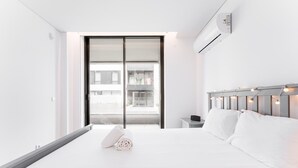 A modern hotel room with a large bed, a nightstand, a wall-mounted air conditioner, and a sliding glass door leading to a balcony. - GuestReady - Amazing Modern home near the beach (Vila Nova de Gaia)