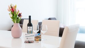 A table with a pink vase of flowers, a bottle of wine, two wine glasses, and a welcome card for Porto. - GuestReady - Amazing Modern home near the beach (Vila Nova de Gaia)