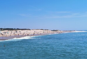 A wide beach with people enjoying the water, a clear sky, and a calm sea.