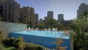 A swimming pool with lounge chairs, surrounded by greenery and tall buildings in the background. - Beautiful apartment, comfortable with excellent location (Santiago)
