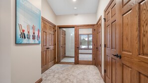Un pasillo con puertas de madera y suelo alfombrado, que conduce a una habitación con vista a una casa a través de un ventanal.