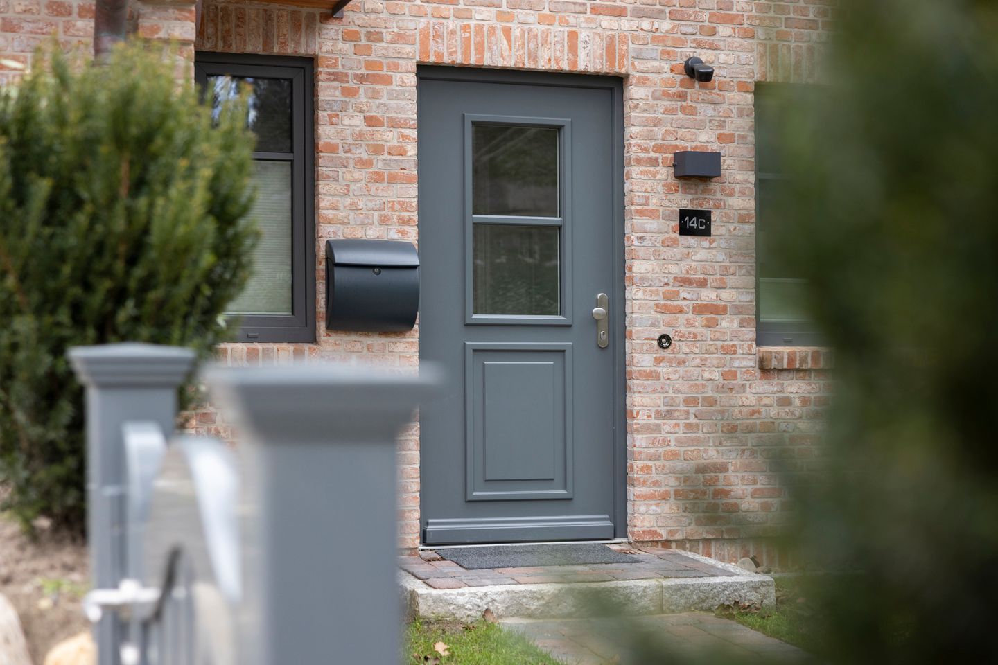 A residential house with a grey door, a mailbox, and a small brick wall.