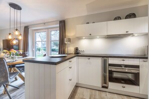 A modern kitchen with white cabinetry, a built-in oven, and a dining area with a table and chairs.