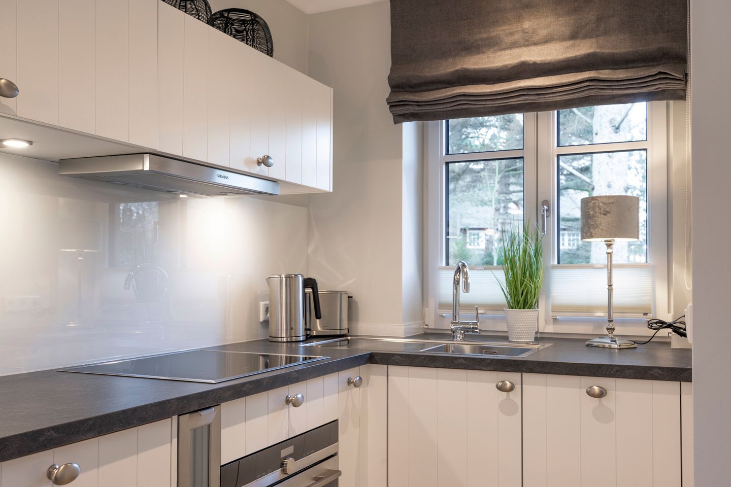 A modern kitchen with white cabinets, stainless steel appliances, and a window with a view of trees.