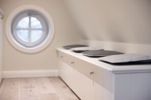 A bedroom with a white dresser, a round window, and a sloped ceiling.