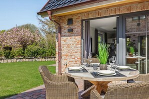 An outdoor dining area with a brick wall, a round table set for four, wicker chairs, and a potted plant.