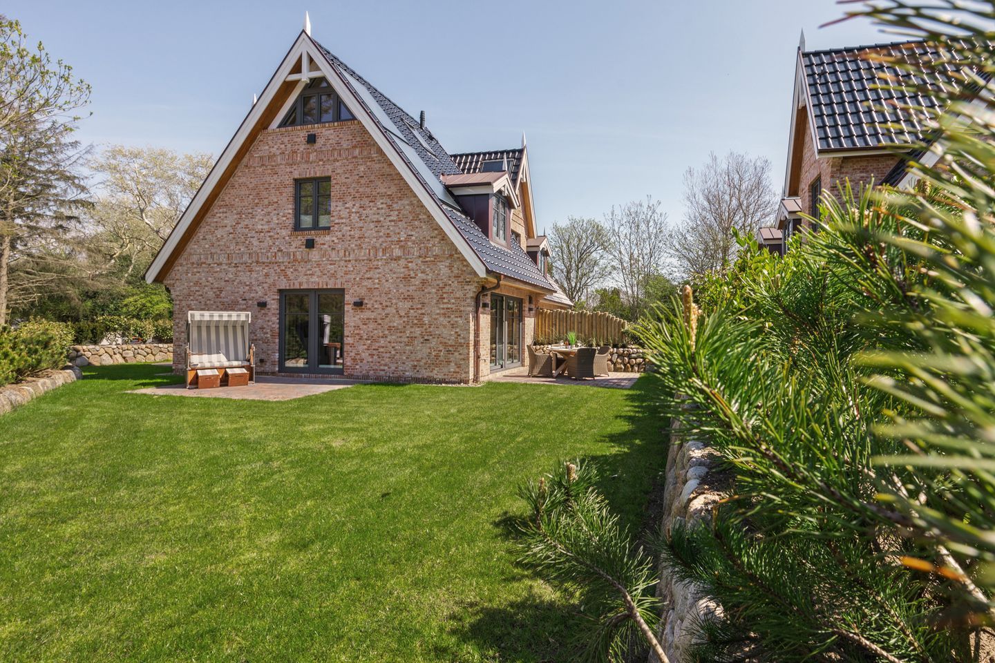 Ein Backsteinhaus mit geneigtem Dach, einer Veranda mit Bank und einem gepflegten Rasen.