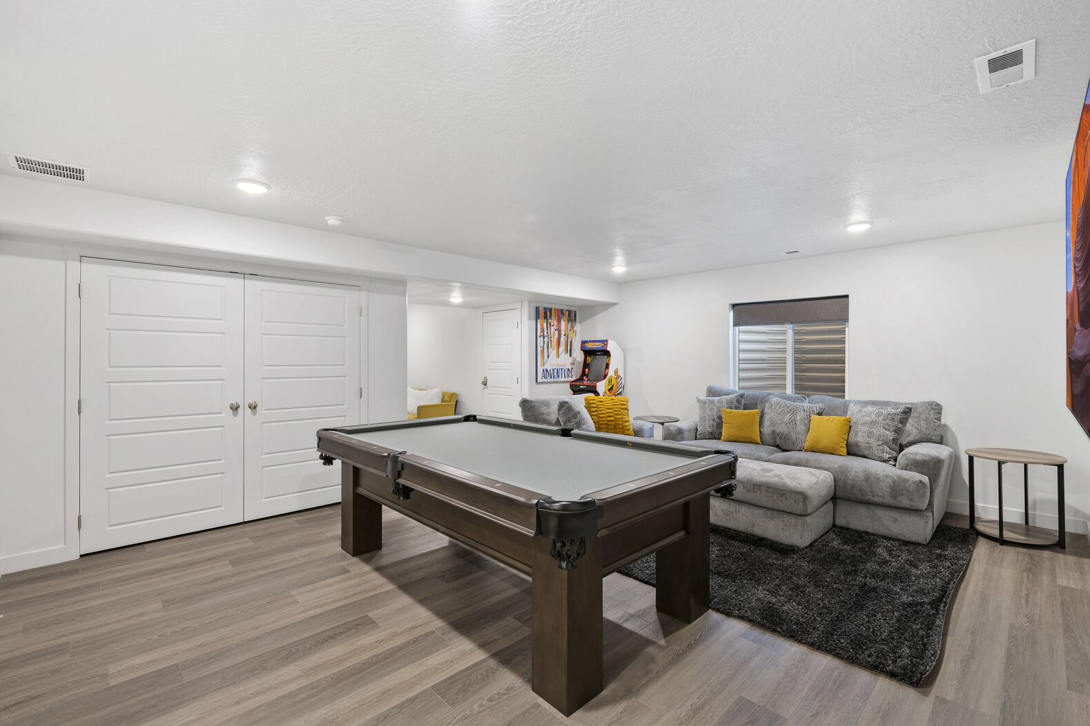 Un salón moderno con mesa de billar, sofá gris con cojines amarillos y una mesita auxiliar.